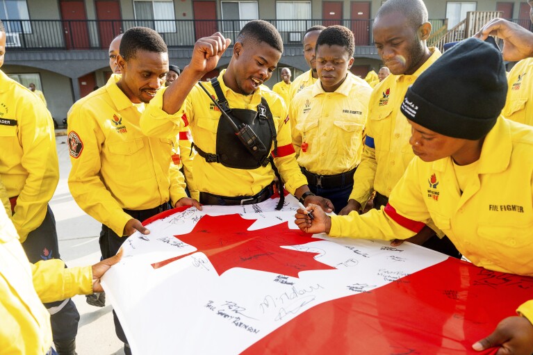 South African firefighters sign a flag given to them by Canadian firefighters in Fox Creek, Alberta, on Tuesday, July 4, 2023. (AP Photo/Noah Berger)