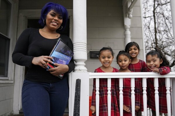 Dinora Torres, a MassBay Community College student, poses with her four daughters on the front porch of their home, Thursday, Jan. 14, 2021, in Milford, Mass. At the college, applications for meal assistance scholarships have increased 80% since last year. Among the recipients is Torres, who said the program helped keep her enrolled.  From front left are daughters Davina, Alana and Hope, with Faith in Dinora's arms. (AP Photo/Charles Krupa)