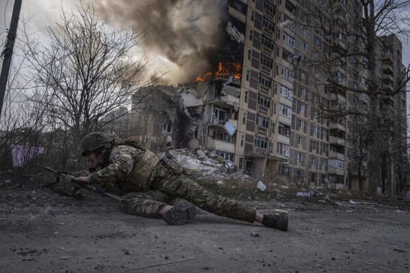A Ukrainian police officer takes cover in front of a burning building that was hit in a Russian airstrike in Avdiivka, Ukraine, Friday, March 17, 2023. (APPhoto/Evgeniy Maloletka)