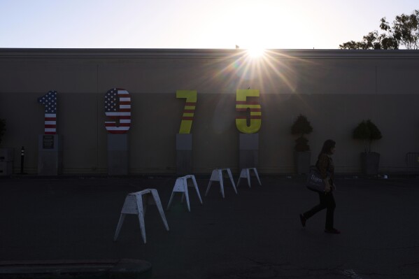 A woman walks past a "1975" installation in the parking lot of Asian Garden Mall as the sun sets behind it in the Little Saigon neighborhood of Westminster, Calif., Monday, April 21, 2025. The display marks the year of the fall of Saigon. (AP Photo/Jae C. Hong)