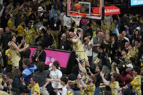 FILE - Wake Forest's Cameron Hildreth (2) drives to the basket as fans storm the court at the end of an NCAA college basketball game against Duke in Winston-Salem, N.C., Saturday, Feb. 24, 2024. Recent incidents in college basketball have underscored the potential dangers that come from jubilant fans storming the court after the game comes to an end. Finding a solution is proving to be a challenge. (AP Photo/Chuck Burton, File)