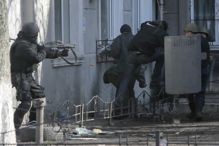 FILE - In this file photo taken on Feb. 18, 2014, a riot police officer shoots during clashes with protesters outside Ukraine's parliament in Kyiv, Ukraine. (AP Photo/Efrem Lukatsky, file)