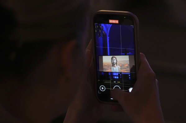 A person takes a video with a cellphone during an AI-created service at St. Paul's Lutheran church in Helsinki, Finland, Tuesday, March 4, 2025.