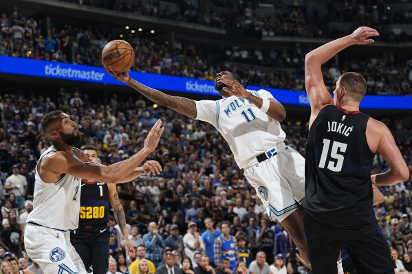 Minnesota Timberwolves center Naz Reid, center, drives to the basket past Denver Nuggets center Nikola Jokic, right, as Minnesota center Rudy Gobert looks on in the second half of Game 7 of an NBA second-round playoff series, Sunday, May 19, 2024, in Denver. (AP Photo/David Zalubowski)
