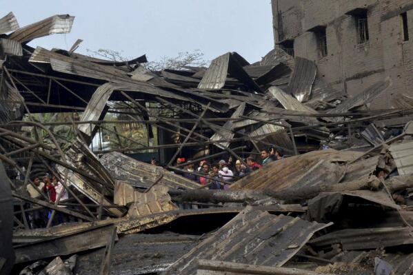 People watch the remains of the food snacks factory that got damaged in an explosion in an industrial area in Muzaffarpur, India, Sunday, Dec. 26, 2021. Police say a factory boiler has exploded in eastern India, killing at least six workers and injuring six others. (AP Photo)
