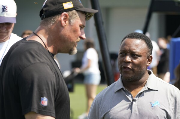 FILE - Detroit Lions head coach Dan Campbell, left, talks with former Lions running back Barry Sanders after an NFL football practice, Tuesday, Aug. 8, 2023, in Allen Park, Mich. “Bye Bye Barry”looks back at Sanders 10-year career with the Lions and his decision to retire in 1999 despite being on the cusp of becoming the NFL's all-time leading rusher. (AP Photo/Carlos Osorio)