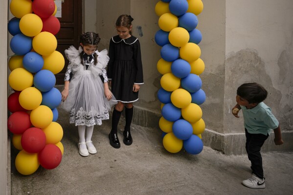 FILE.- A boy watches Ukrainian refugee girls posing for pictures between balloons in the colors of the Ukrainian and Romanian flags at the Ienachita Vacarescu Elementary School in Bucharest, Romania, Monday, Sept. 5, 2022. As a woman photojournalist, Andreea says " I, much like every woman, often feel some level of discrimination, either manifested openly or in a more veiled manner. However, that is nowhere near what women face in disadvantaged social groups where access to education is not a given or minimum decent living conditions are not met."(AP Photo/Andreea Alexandru, File)