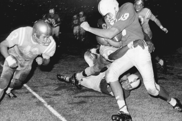 North Carolina State quarterback Roman Gabriel is in the clutches of a UCLA player as another is driving in at left as he was stopped after an end sweep during an NCAA college football game Oct. 29, 1960, in Los Angeles. Gabriel, the former North Carolina State quarterback who was the 1969 NFL MVP with the Los Angeles Rams, died Saturday, April 20, 2024. He was 83. (AP Photo/Harold P. Matosian)
