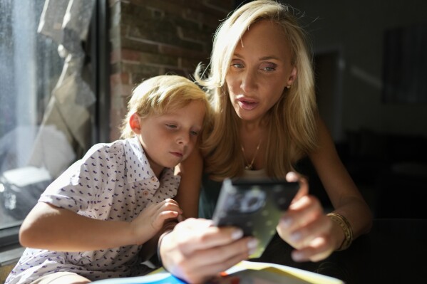 Florida state Sen. Lauren Book and her six-year-old son Hudson look at a phone app which provides real-time rocket alerts to Israeli citizens, Oct. 24, 2023, in Plantation, Fla. Book follows the alerts to stay informed and help her children understand what is happening. "I don't want to forget. I don't want my children to ever forget. I don't want my community to forget." (AP Photo/Rebecca Blackwell)