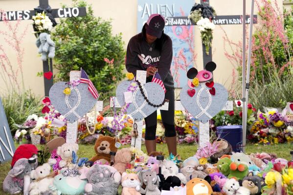 Inga VanWagoner, of Allen, Texas, who served in he U.S. Army, places flags atop crosses at a makeshift memorial by the mall where several people were killed, Wednesday, May 10, 2023, in Allen, Texas. (AP Photo/Tony Gutierrez)