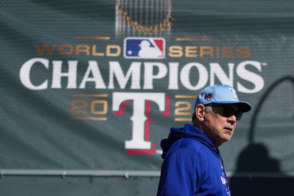 Texas Rangers manager Bruce Bochy walks by a 2023 World Series champions banner before his team's spring training baseball workouts Wednesday, Feb. 14, 2024, in Surprise, Ariz. (AP Photo/Lindsey Wasson)
