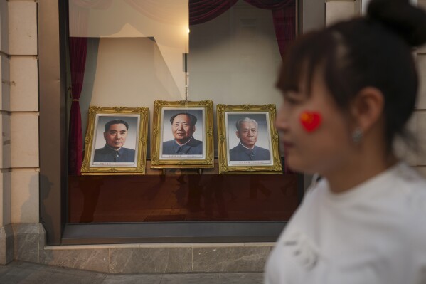 A woman walks past portraits of late Chinese leaders including Mao Zedong at the Wangfujing Shopping street in Beijing, China, Thursday, April 11, 2024. (AP Photo/Tatan Syuflana)
