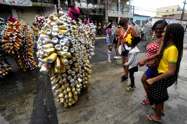 Locals watch revelers wearing costumes made from beer and soda cans during the 'Bloco da Latinha' street party Carnival parade in Madre de Deus, Brazil, Sunday, Feb. 11, 2024. (AP Photo/Eraldo Peres)