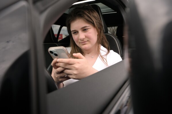 Alexis Bogan, whose speech was impaired by a brain tumor, uses an AI powered smartphone app to create a audible drink order at a Starbucks drive-thru on Monday, April 29, 2024, in Lincoln, R.I. The app converts her typed entries into a verbal message created using her original voice. (AP Photo/Steven Senne)