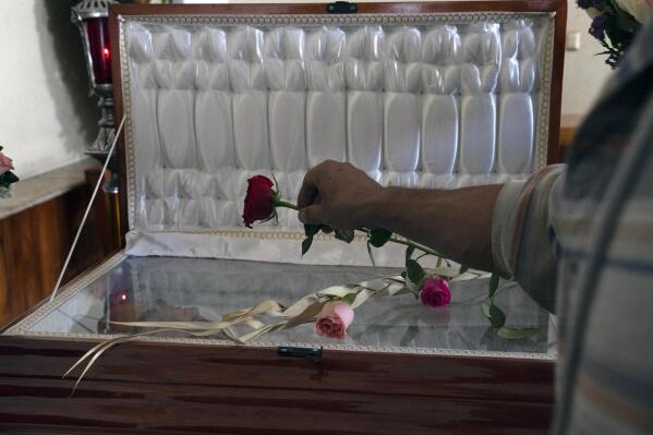 A friend places a rose on the open-faced casket that contains the remains of slain journalist Armando Linares in Zitacuaro, in the state of Michoacan, Mexico, Wednesday, March 16, 2022. Linares was shot to death at a home in the town of Zitacuaro on Tuesday, the eighth Mexican journalist murdered so far this year. (AP Photo/Marco Ugarte)