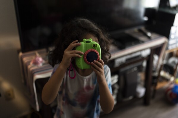 Rubie Caceres, a granddaughter of Marina Maalouf, a longtime resident of Hillside Villa, plays with a toy camera in her apartment in Los Angeles, Tuesday, Oct. 1, 2024. (AP Photo/Jae C. Hong)