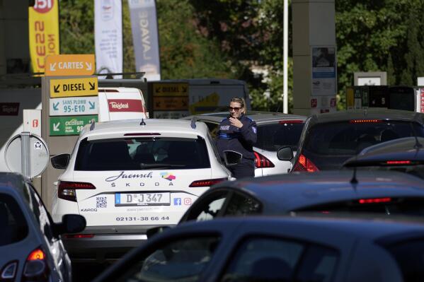 A police officer directs cars as drivers line up in a gas station in Paris, Tuesday, Oct.11, 2022. Shortages which the government says are largely caused by strikes that have hit French fuel refineries are making life difficult for drivers in the Paris region and elsewhere. (AP Photo/Christophe Ena)
