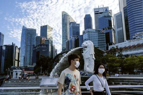 In this March 14, 2020, photo, a couple wearing face masks walk past the Merlion statue in Singapore. As the virus outbreak spreads ever further, it's becoming clear that some strategies are more likely to succeed in containing it: pro-active efforts to track down and isolate cases, access to basic, affordable public health and clear, reassuring messaging from leaders. (AP Photo/Ee Ming Toh)