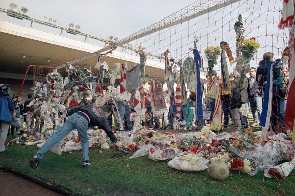 FiLE - In this file photo dated April 16, 1989, a Liverpool Football Club fan places a pair of football boots in the goal at the Kop end of Anfield Stadium as hundreds came to mourn the loss of fellow Liverpool fans.  Liverpool players and staff have observed 97 seconds of silence in honor of Andrew Devine. The lifelong fan died Tuesday, July 27, 2021 from long-term injuries sustained in the Hillsborough disaster. He was 55.  (AP Photo/Peter Kemp, File)