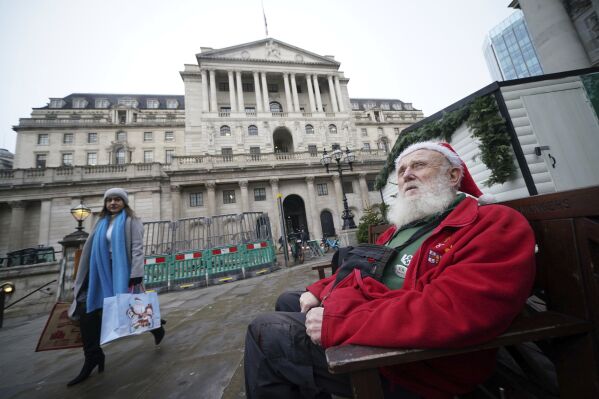 Gerard White, wearing a Santa hat and waiting for his wife to finish work, sits outside the Bank of England, which is expected to hold interest rates for the third time in a row, as fresh data has pointed towards potential cracks in the economy, in London, Thursday Dec. 14, 2023. (Yui Mok/PA via AP)