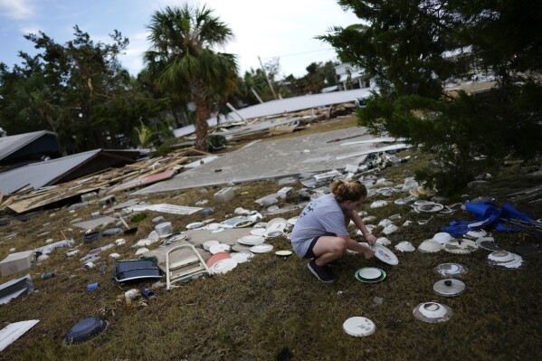 Lainey Hamelink, 9, whose family owned the property next door, helps to collect scattered dishes at Tina's Dockside Inn, which was completely destroyed in Hurricane Idalia, in Horseshoe Beach, Fla., Friday, Sept. 1, 2023, two days after the storm's passage. (AP Photo/Rebecca Blackwell)
