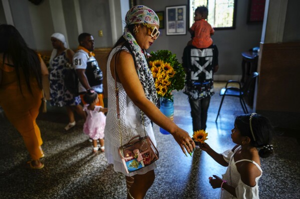 A mother and daughter prepare to make an offering of sunflowers to the Virgin of Charity of Cobre at her shrine in El Cobre, Cuba, Sunday, Feb. 11, 2024. The Vatican-recognized Virgin, venerated by Catholics and followers of Afro-Cuban Santeria traditions, is at the heart of Cuban identity, uniting compatriots from the Communist-run Caribbean island to those who were exiled or emigrated to the U.S. (AP Photo/Ramon Espinosa)