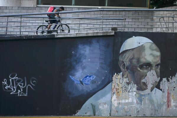 FILE - A cyclists pedals his bike up a ramp near a weathered mural of Pope Francis, in Buenos Aires, Argentina, Thursday, March 2, 2023. Francis left Argentina in February 2013 to attend the conclave that elected him as the successor to Benedict XVI on March 13. (AP Photo/Natacha Pisarenko, File)