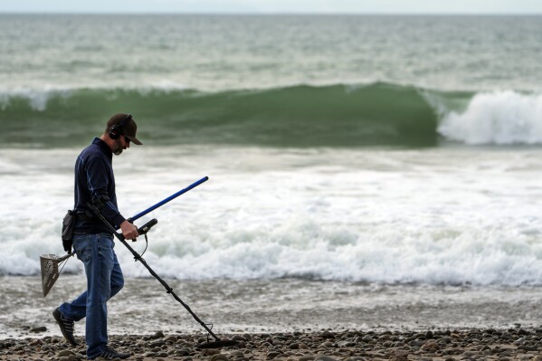 Josh Snider searches for metals with a metal detector on the edge of the beach ahead of storms, Wednesday, Jan. 31, 2024, in Ventura, Calif. The first of two back-to-back atmospheric rivers slowly pushed into California on Wednesday, triggering statewide storm preparations and calls for people to get ready for potential flooding, heavy snow and damaging winds. (AP Photo/Damian Dovarganes)