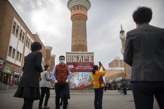 FILE - Tourists take photos near a tower at the International Grand Bazaar in Urumqi in western China's Xinjiang Uyghur Autonomous Region, as seen during a government organized trip for foreign journalists on April 21, 2021. Some U.S. lawmakers are demanding that seafood processed in two Chinese provinces be banned from entering the U.S. market. It's the latest effort by lawmakers to restrict imports of Chinese goods on the grounds of rights abuse, a move that is certain to irk Beijing at a time of tensions over trade and other issues. (AP Photo/Mark Schiefelbein, File)