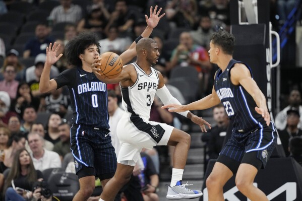 San Antonio Spurs guard Chris Paul (3) drives between Orlando Magic guard Anthony Black (0) and forward Tristan da Silva (23) during the first half of a preseason NBA basketball game in San Antonio, Wednesday, Oct. 9, 2024. (AP Photo/Eric Gay)