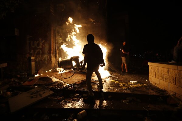 EDS NOTE: OBSCENITY - Protesters add fuel to a fire at the Minneapolis police 3rd Precinct building Thursday, May 28, 2020, in Minneapolis. Violent protests over the death of George Floyd, a black man who died in police custody Monday, broke out in Minneapolis for a third straight night. (AP Photo/John Minchillo)