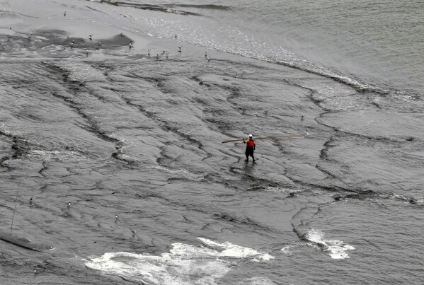 FILE - A worker walks through the water as a berm system is constructed in the aftermath of the gulf oil spill on the northern end of the Chandeleur Islands, La., July 15, 2010. When a deadly explosion destroyed BP's Deepwater Horizon drilling rig in the Gulf of Mexico, tens of thousands of ordinary people were hired to help clean up the environmental devastation. (AP Photo/Dave Martin, File)