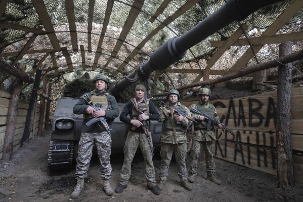 Ukrainian servicemen of the 92nd separate assault brigade pose for photo at their 155mm M-109 "Paladin" howitzer on the frontline near Vovchansk, Kharkiv region, Ukraine, Monday, Oct. 28, 2024, with sign in the background reads "Glory to Ukraine". (AP Photo/Efrem Lukatsky)