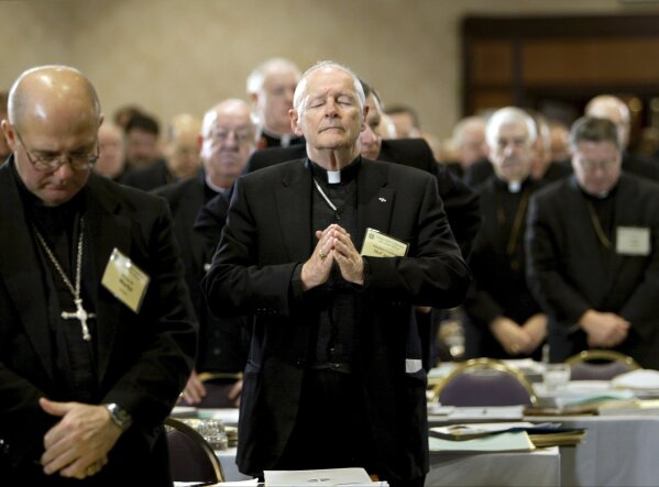 FILE - In this Nov. 10, 2003 file photo, Cardinal Theodore Edgar McCarrick, Archbishop of Washington, D.C., center, joins his fellow clergy in prayer at the end of the opening session of the U.S. Conference of Catholic Bishops meeting in Washington. On Tuesday, Nov. 10, 2020, the Vatican is taking the extraordinary step of publishing its two-year investigation into the disgraced ex-Cardinal McCarrick, who was defrocked in 2019 after the Vatican determined that years of rumors that he was a sexual predator were true. (AP Photo/J. Scott Applewhite, File)