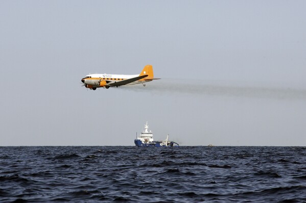 FILE - A plane drops chemicals to help disperse oil from a leaking pipeline that resulted from last week's explosion and collapse of the Deepwater Horizon oil rig in the Gulf of Mexico near the coast of Louisiana, April 27, 2010. When the deadly explosion destroyed the rig in the Gulf of Mexico, tens of thousands of ordinary people were hired to help clean up the environmental devastation. These workers were exposed to crude oil and the chemical dispersant Corexit. (AP Photo/Patrick Semansky, File)