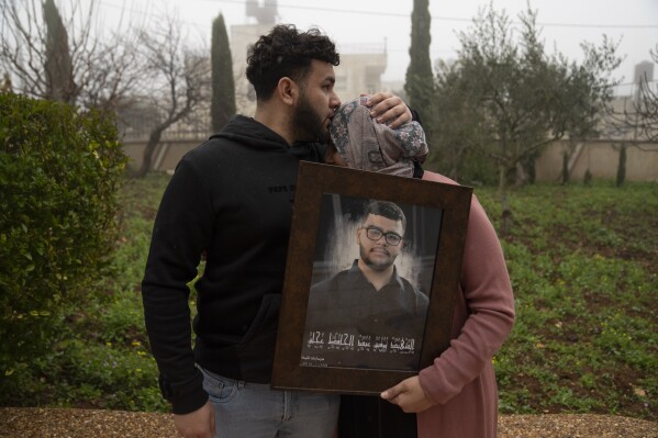 Amir Abdel Jabbar, whose younger brother Tawfic was fatally shot last week, comforts their mother, Mona, while she poses with a framed photo of the family in their home village of Al-Mazra'a ash-Sharqiya, West Bank, Tuesday, Jan. 23, 2024. Tawfic was from Louisiana, and the White House has demanded a transparent investigation into the death. (AP Photo/Nasser Nasser)