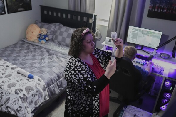 Jessica Blazier, center, prepares an infusion for her son, Julian, right, Wednesday, April 9, 2025, in Bloomfield, Ind. (AP Photo/Joshua A. Bickel)