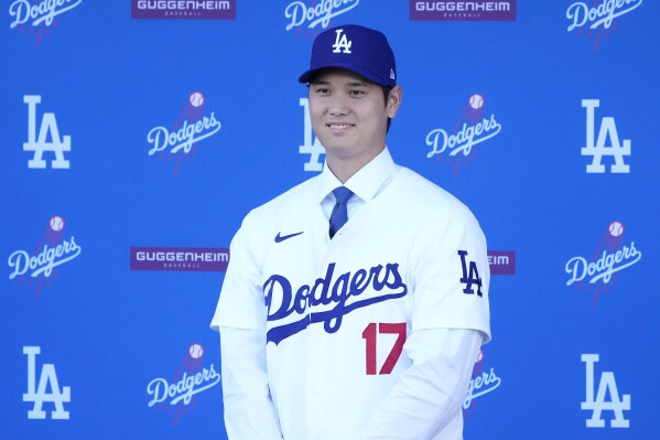 Los Angeles Dodgers' Shohei Ohtani smiles while wearing a jersey and baseball cap during a news conference at Dodger Stadium Thursday, Dec. 14, 2023, in Los Angeles. (AP Photo/Marcio Jose Sanchez)