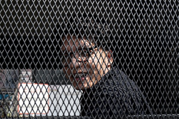 Freelance photographer Natthapon Phanphongsanon sits in a police van at Thing Song Hong police station in Bangkok, Thailand, Tuesday, Feb. 13, 2024. He was one of two journalists arrested in connection with their coverage of a political activist who spray-painted graffiti on the wall of Bangkok's Grand Palace last year. Both were freed on bail on Tuesday. (AP Photo/Tananchai Keawsowattana)