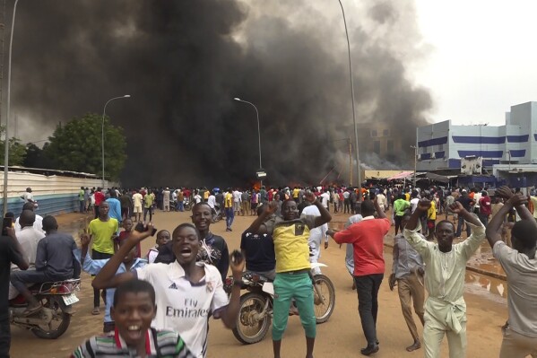 With the headquarters of the ruling party burning in the back, supporters of mutinous soldiers demonstrate in Niamey, Niger, Thursday, July 27 2023. Governing bodies in Africa condemned what they characterized as a coup attempt Wednesday against Niger's President Mohamed Bazoum, after members of the presidential guard declared they had seized power in a coup over the West African country's deteriorating security situation. (AP Photo/Fatahoulaye Hassane Midou)