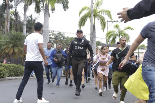 Police evacuate staff from the TC public television station after a group of armed men broke onto their set during a live broadcast, in Guayaquil, Ecuador, Tuesday, Jan. 9, 2024. The country has seen a series of attacks after the government imposed a state of emergency in the wake of the apparent escape of a powerful gang leader from prison. (AP Photo/Cesar Munoz)