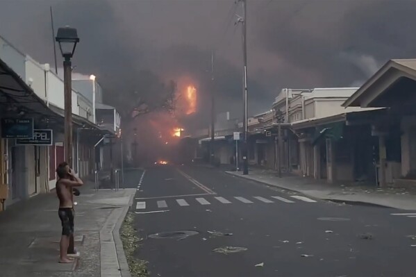 People watch as smoke and flames fill the air from raging wildfires on Front Street in downtown Lahaina, Maui on Tuesday, Aug. 8, 2023. Maui officials say wildfire in the historic town has burned parts of one of the most popular tourist areas in Hawaii. County of Maui spokesperson Mahina Martin said in a phone interview early Wednesday says fire was widespread in Lahaina, including Front Street, an area of the town popular with tourists. (Alan Dickar via AP