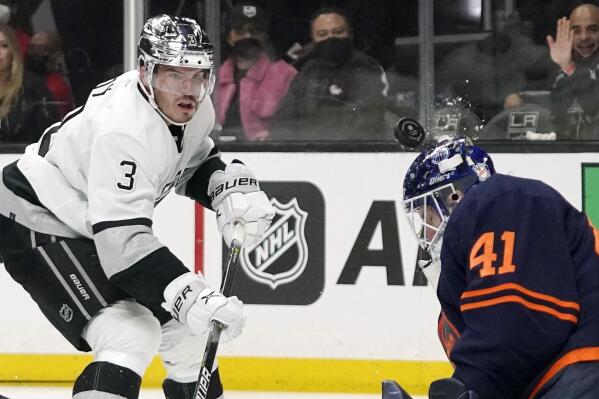 A shot by Los Angeles Kings defenseman Matt Roy, left, hits Edmonton Oilers goaltender Mike Smith in the helmet during the second period of an NHL hockey game Tuesday, Feb. 15, 2022, in Los Angeles. (AP Photo/Mark J. Terrill)