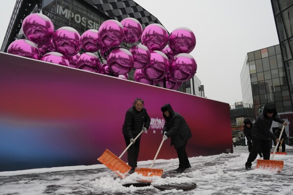 Workers sweep snow into a manhole near a decoration setup ahead of the Christmas festival at a mall in Beijing, Thursday, Dec. 14, 2023. China's economy will slow next year, with annual growth falling to 4.5% from 5.2% this year despite a recent recovery spurred by investments in factories and construction and in demand for services, The World Bank said in a report issued Thursday. (AP Photo/Ng Han Guan)