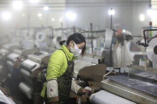 In this Feb. 27, 2020 photo, a woman works on a spinning mill in a textile factory in Hangzhou in eastern China's Zhejiang Province. A gauge of Chinese manufacturing plunged in February by an even wider margin than expected after efforts to contain a virus outbreak shut down much of the world's second-largest economy. (Chinatopix via AP)