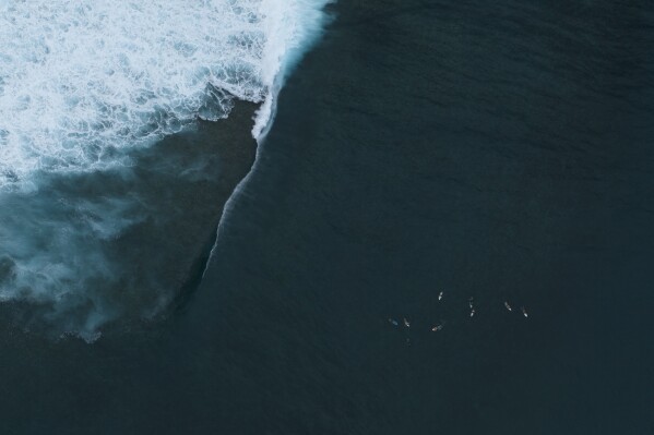 Surfers gather in the water as a wave breaks over the coral reef in Teahupo'o, Tahiti, French Polynesia, Saturday, Jan. 13, 2024. (AP Photo/Daniel Cole)