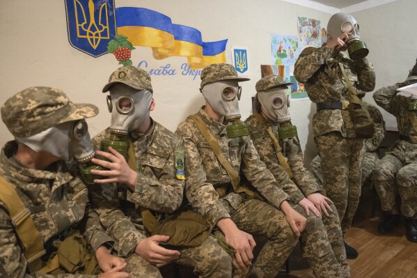 Cadets practice putting on gas masks during a lesson in a bomb shelter in a cadet lyceum in Kyiv, Ukraine, Tuesday, June 6, 2023. Writing on the wall reads: "Glory to Ukraine". (AP Photo/Efrem Lukatsky)