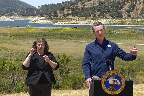 FILE - In this July 8, 2021, file photo, California Gov. Gavin Newsom and sign interpreter Julia Townsend stand at the edge of a diminished Lopez Lake near Arroyo Grande, Calif. Newsom threatened Monday, May 23, 2022, to impose mandatory, statewide restrictions on water use if people don't start using less on their own as the drought drags on and the hotter summer months approach. (David Middlecamp/The Tribune of San Luis Obispo via AP, File)