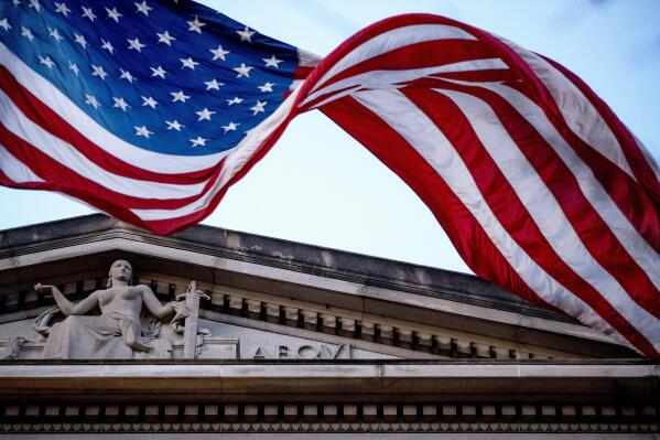 FILE - An American flag flies outside the Department of Justice in Washington, March 22, 2019. The Justice Department says three Iranian citizens have been charged in the United States with cyberattacks that targeted power companies, local governments and small businesses and nonprofits, including a domestic violence shelter. (AP Photo/Andrew Harnik, File)