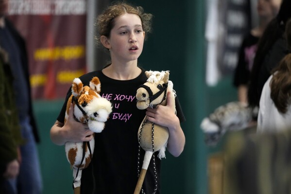A girl carries her hobby horses during a Hobby horsing competition in St. Petersburg, Russia, on Sunday, April 21, 2024. Several dozen kids, 48 girls and one boy, from first-graders to teenagers gathered in a gymnasium in northern St. Petersburg, Russia's second largest city, for a hobby horsing competition. (AP Photo/Dmitri Lovetsky)